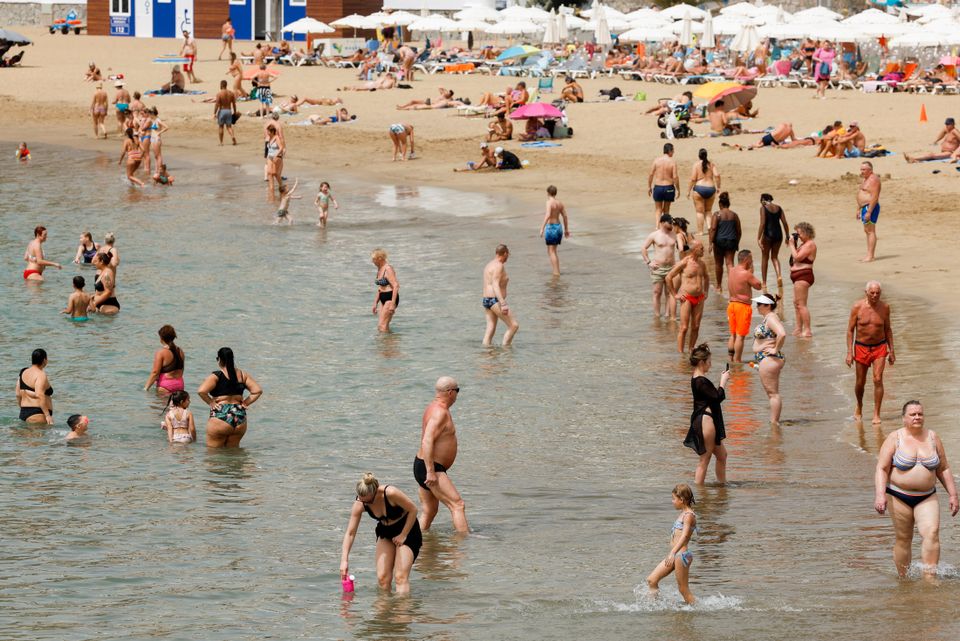 Mange mennesker bader i vannet på en stor strand.