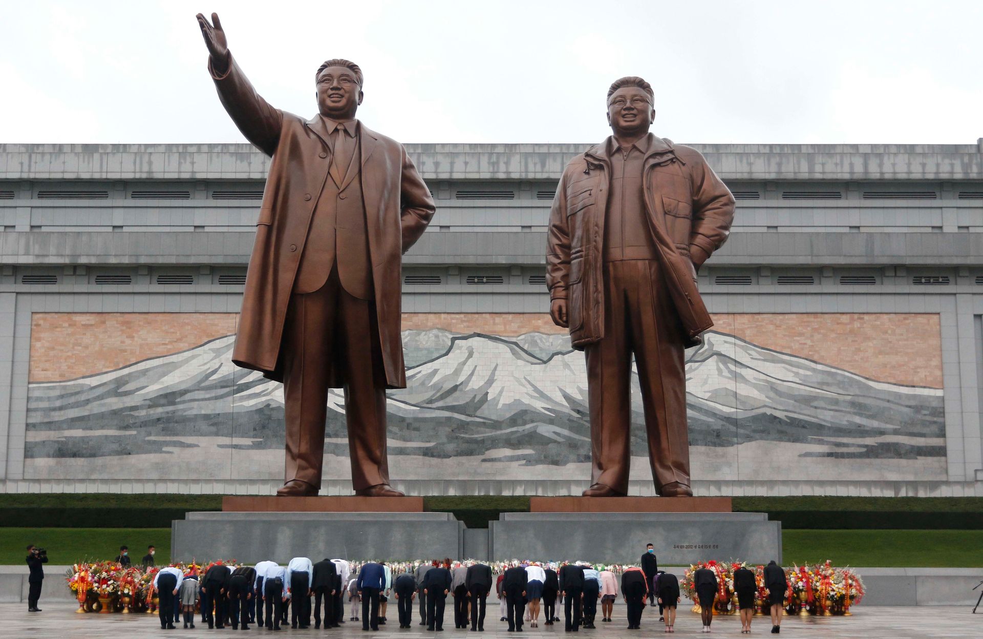 Mange folk bukker foran to statuer i bronse av to menn.
