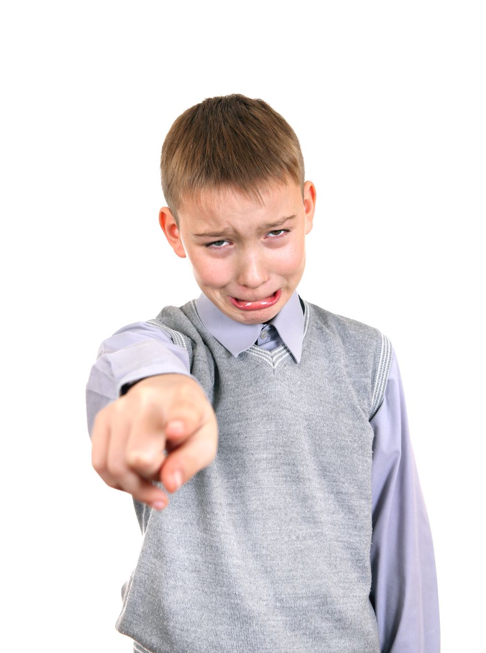 En gutt med kort hår, skjorte og vest står og peker mot fotografen og lager en ukomfortabel, skyldig grimase.