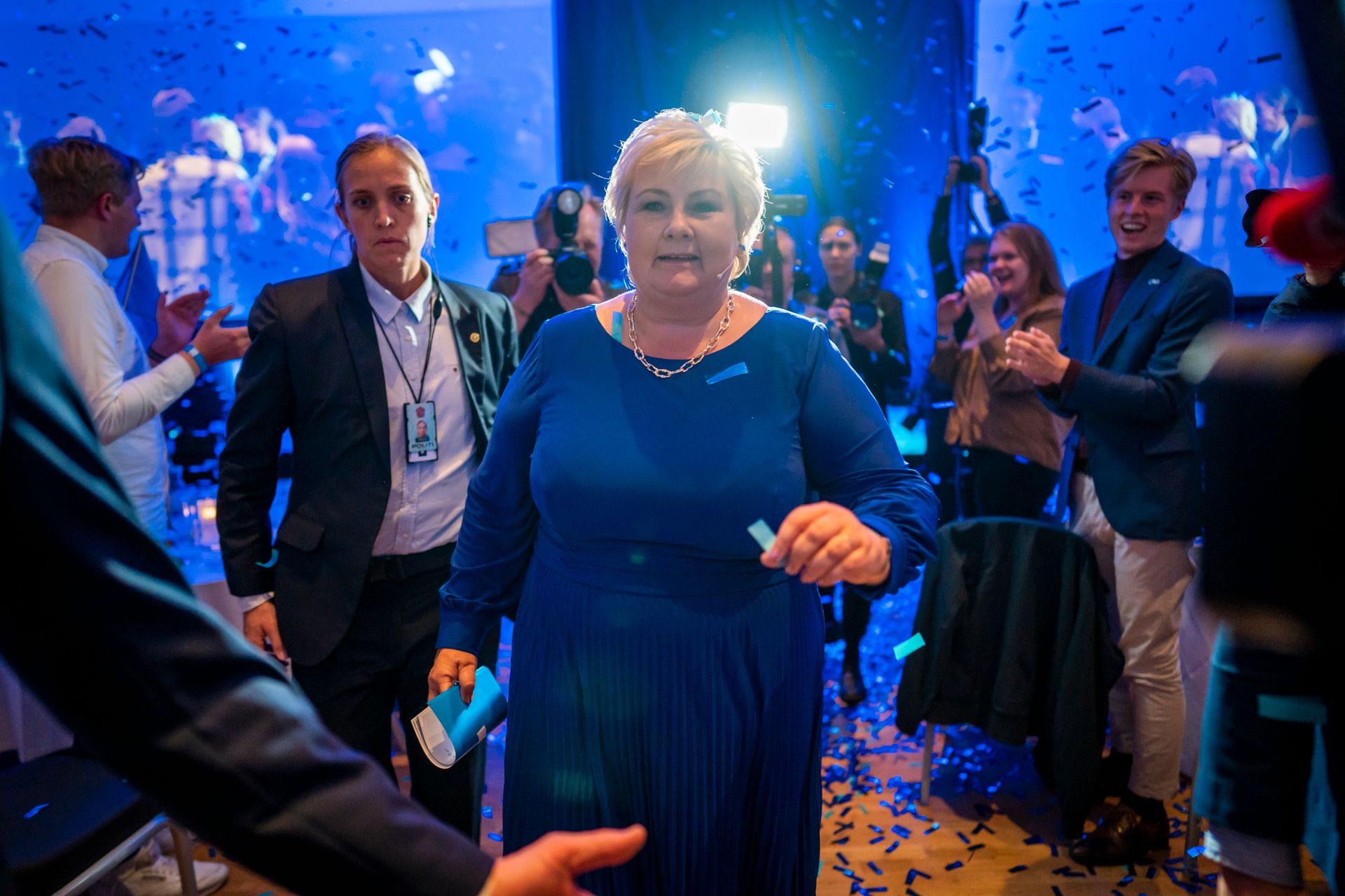 Erna Solberg har på seg en blå kjole og går mot fotografen, på vei ut av den blåpyntede valgvaken til Høyre.