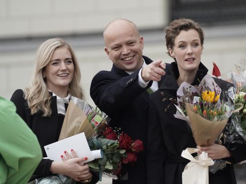En ung, blond kvinne, en dresskledd Trygve Slagsvold Vedum og en kortklippet brunette holder flere blomsterbuketter og smiler mot pressen. 
