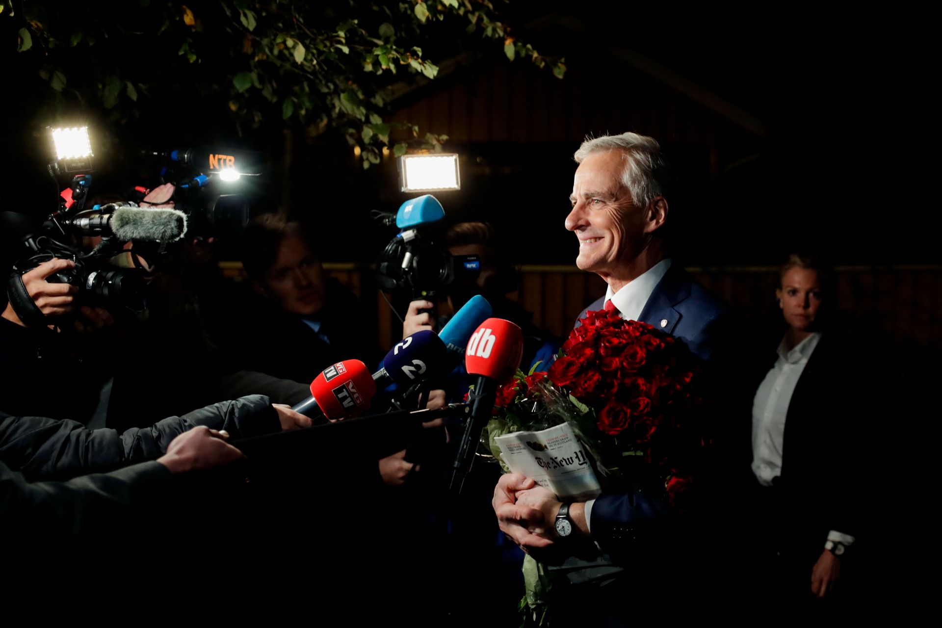 Jonas Gahr Støre smiler, med en stor bukett røde roser i armene, mens kameraer, videolys og mikrofoner strekkes mot ham ute i mørket på vei til Stortinget.