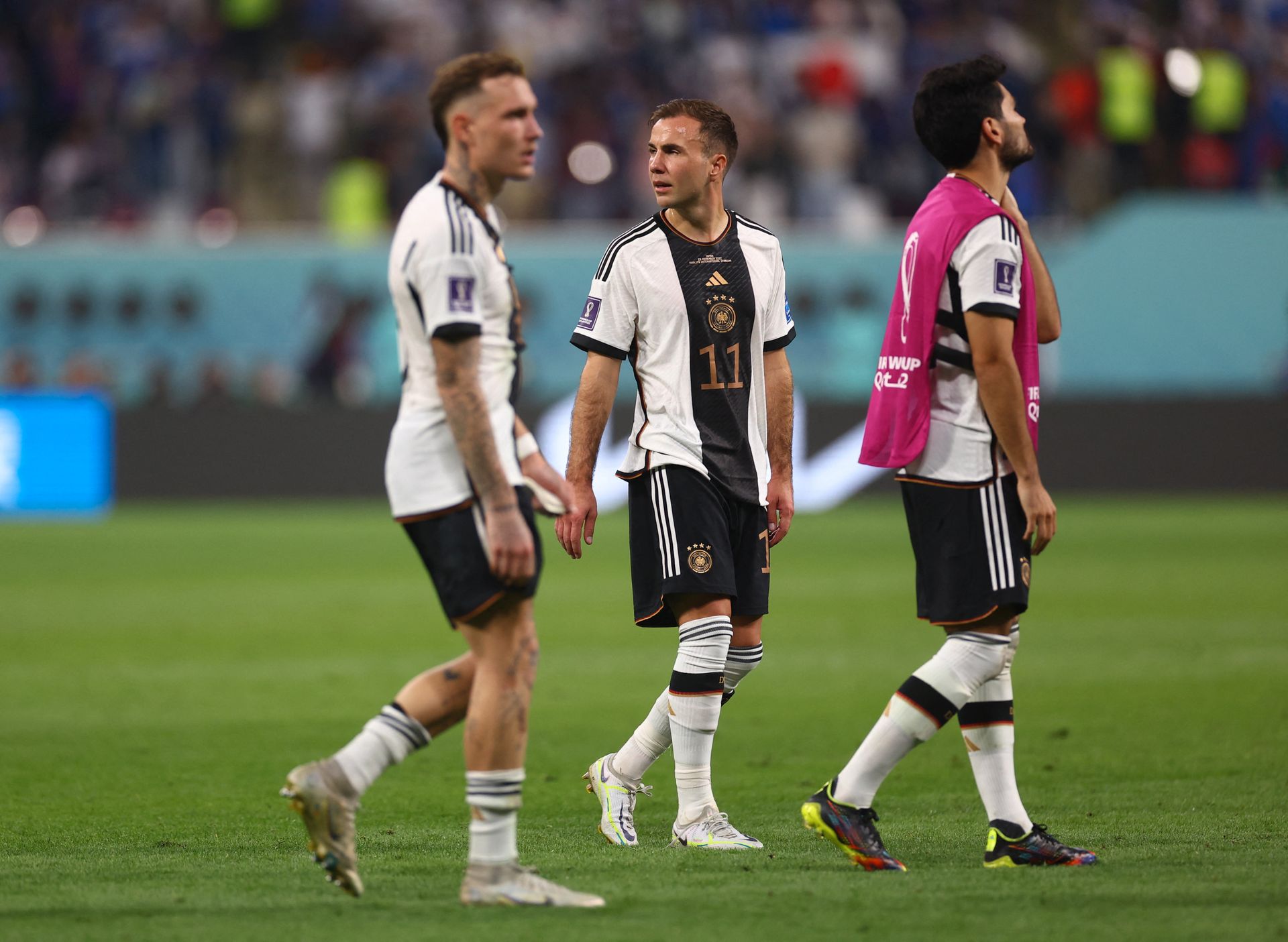 Tre fotballspillere med hvit og svart drakt går skuffet av banen.