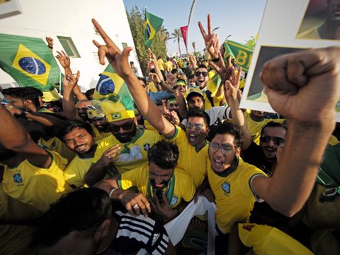 En stor gruppe supportere i gule trøyer og brasilianske flagg jubler og heier ute på gaten.