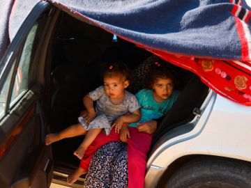 To barn sitter ved siden av hverandre i en bil med et teppe over bildøren.