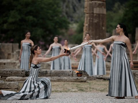 Kvinner med like svarte- og hvitstripete kjoler danser og tenner på en fakkel ved noen ruiner i en skog.