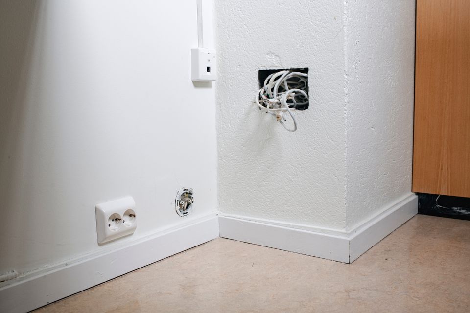 Nærbilde av mange forskjellige ledninger som stikker ut av et hull i en hvit vegg