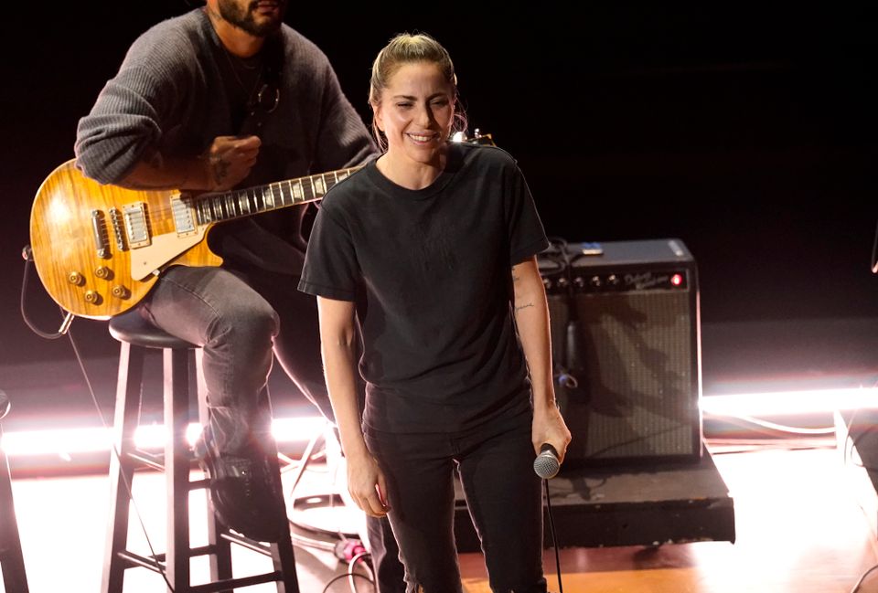 En kvinne med sorte bukser og sort t-skjorte står på scenen og smiler og holder en mikrofon.