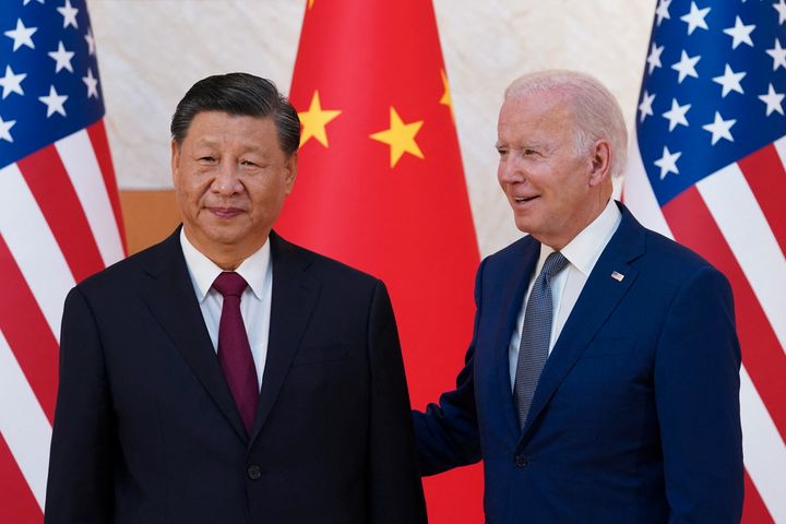 En kinesisk mann i dress og en eldre mann med hvitt hår og dress står foran USAs og Kinas flagg og smiler. 