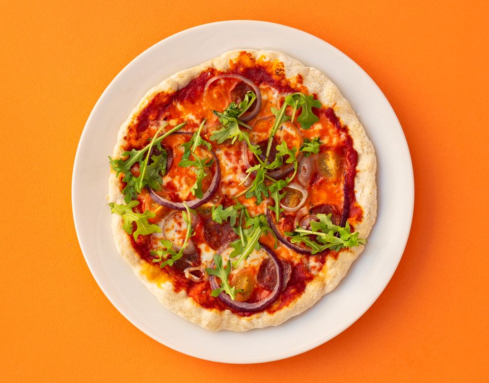Et hvitt fat med en pizza med rød saus og ruccola oppå, ligger på en knalloransje bakgrunn.