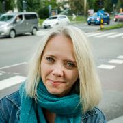 En kvinne i 40-årene med blondt hår står foran en vei med flere biler