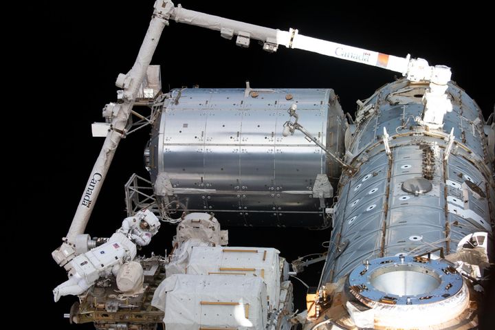 To astronauter i hvit romdrakt henger utenfor en slags romstasjon og gjør reparasjoner, mens det er helt svart rundt dem.