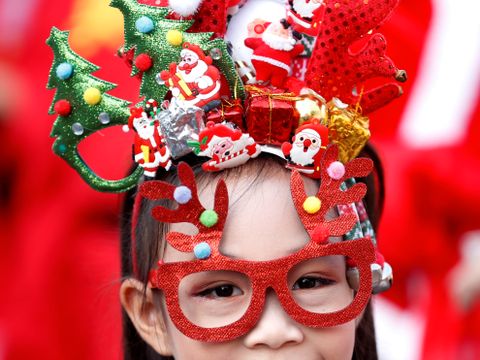 Nærbilde av en jente med røde moro-briller med reinsdyrhorn, julekuler, juletrær og pakker festet på. 