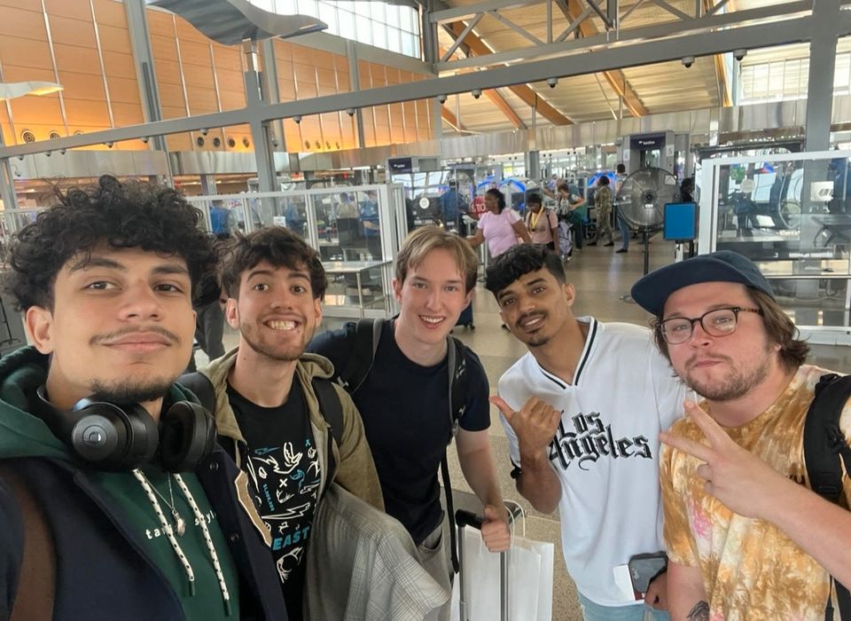 Fem menn står ved siden av hverandre på en flyplass og smiler.