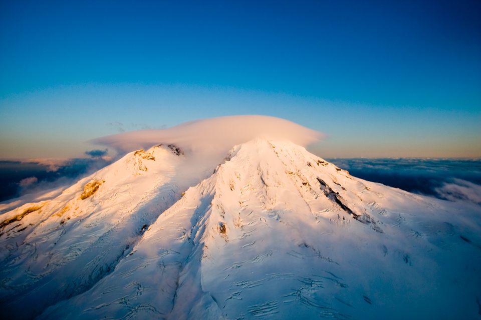 En stor vulkan dekket i hvit snø foran en lysblå himmel.