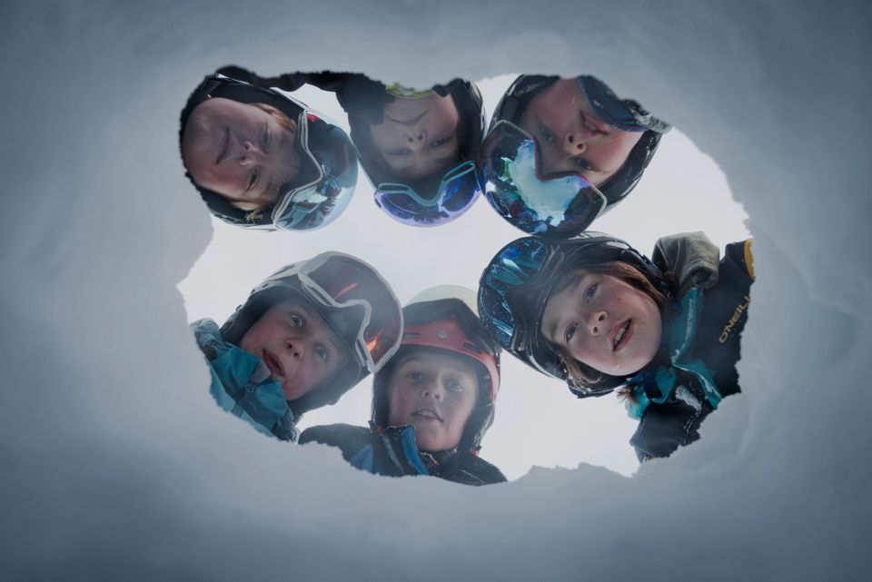 Et bilde som er tatt med kamera under snøen hvor fem gutter kikker ned mot kamera ovenfra. 