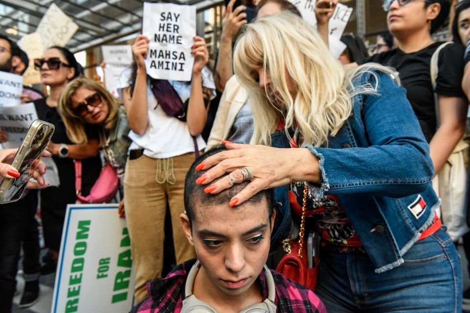 En kvinne blir barbert av håret på mens mange mennesker står rundt og viser frem skilt.