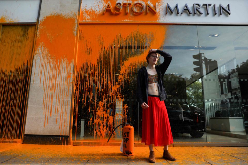 En kvinne med rødt skjørt klær seg til hodet og står foran en butikk som det er kastet masse maling på.