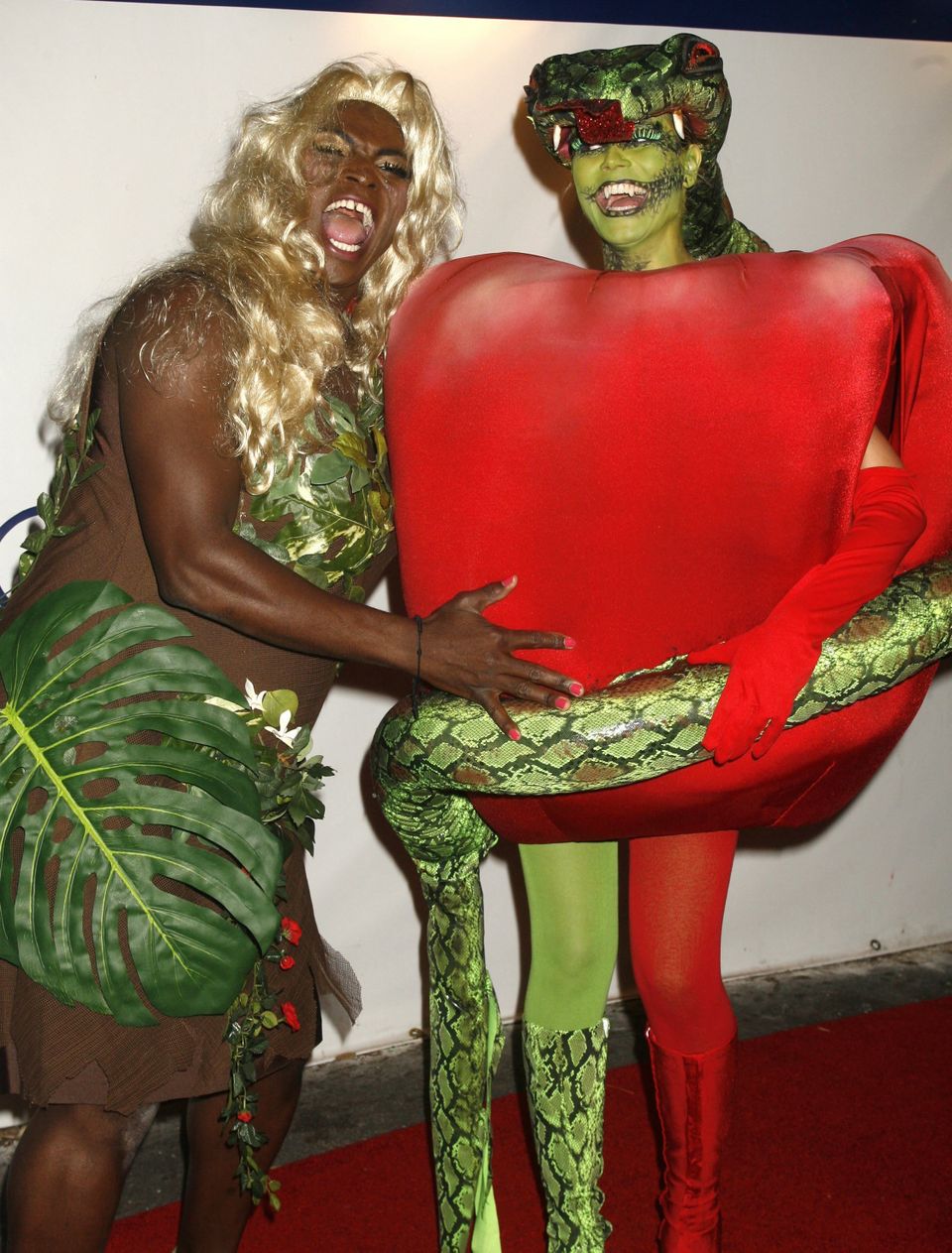 En mann med blond parykk og blader på kroppen holder rundt en kvinne med et stort eple-kostyme og en kunstig slange.