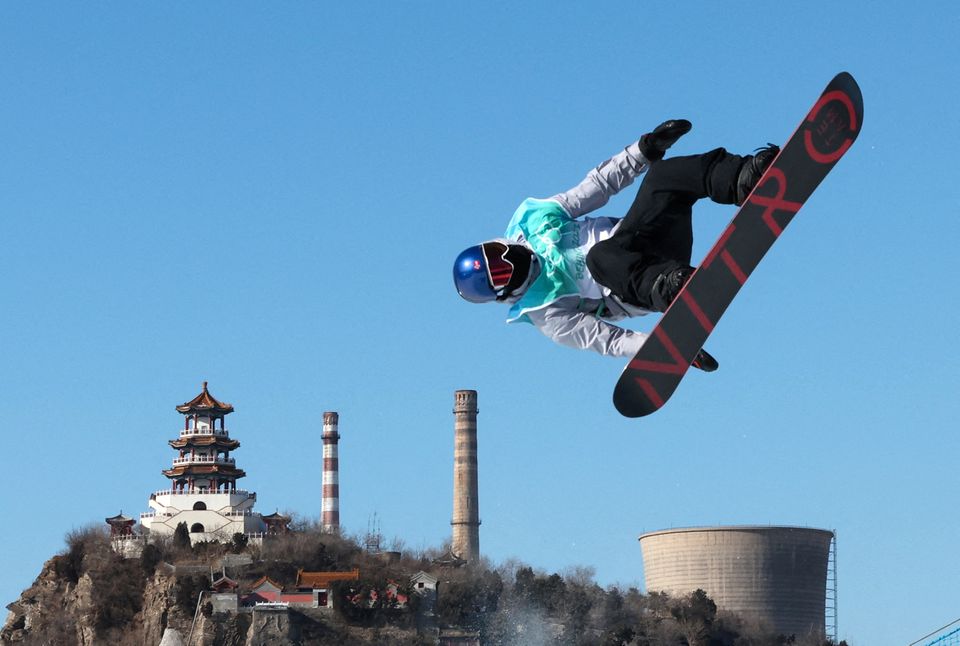 En mann står nesten opp ned på et snowboard i luften med blå hjelm.