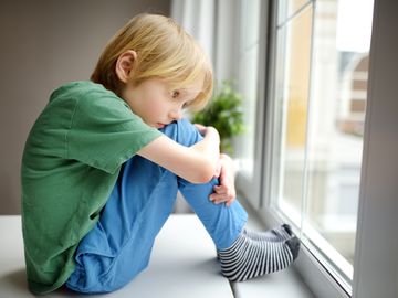 Trist gutt sitter i vinduskarmen