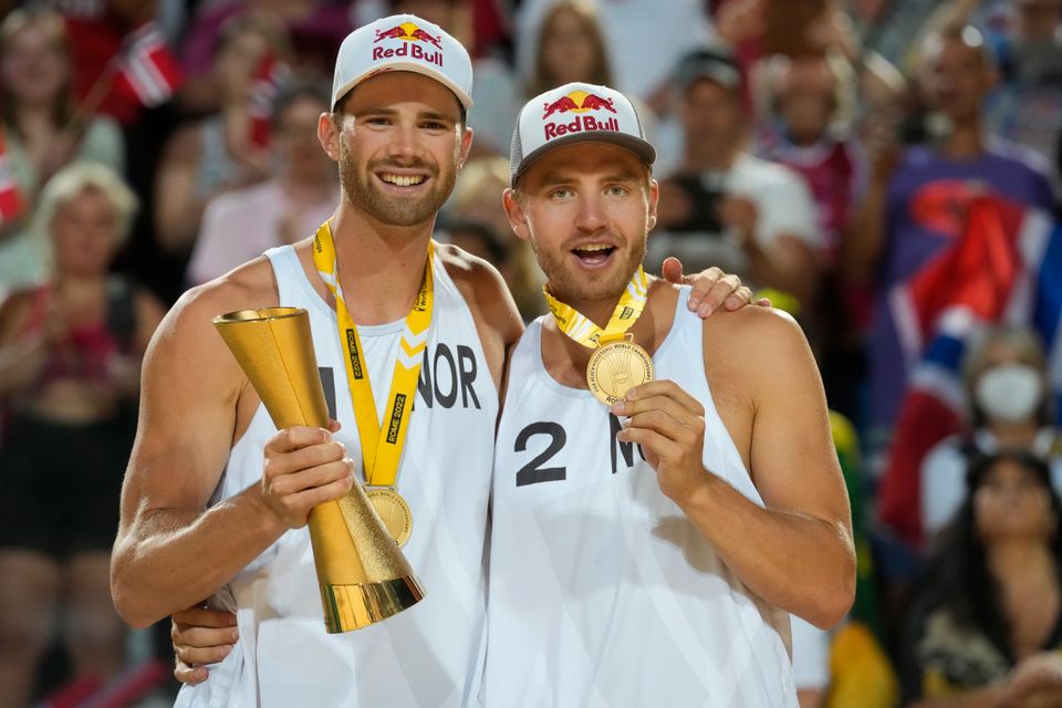 To glade menn i hvite klær har hver sin gullmedalje og den ene holder en pokal.