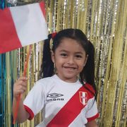 En jente med svarte musefletter og fotballdrakt og flagg i hvitt og rødt smiler mot kameraet. 