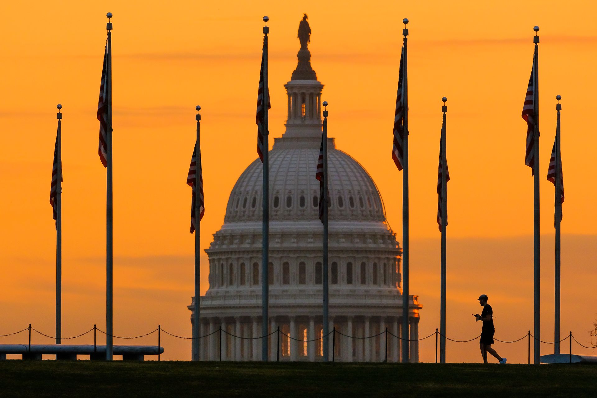 Toppen av Kongressen, en hvit bygning med en slags kuppel øverst ses gjennom flere flaggstenger under en oransje solnedgang.