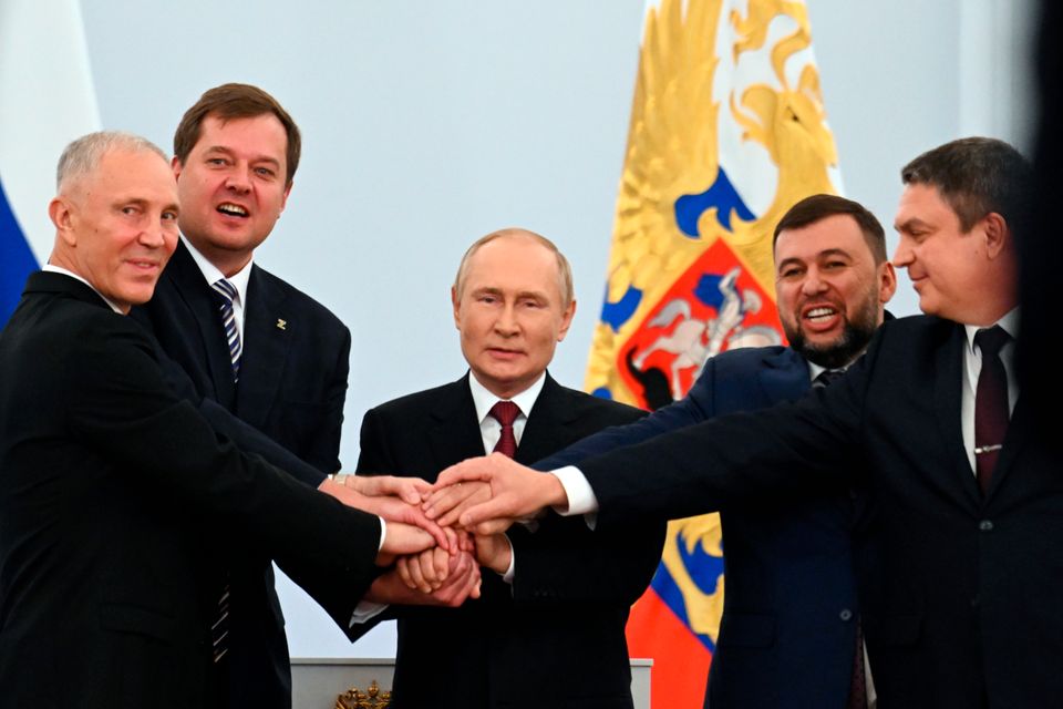 Valdimir Putin står i mellom fire menn i dress og de holder alle hendene sine oppe Putin sin hånd.