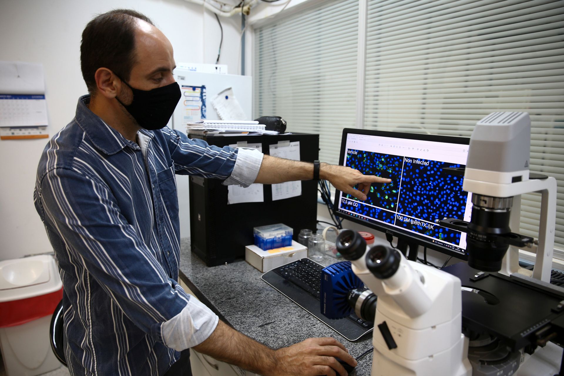 En forsker med munnbind ser og peker på en skjerm med testresultater. 