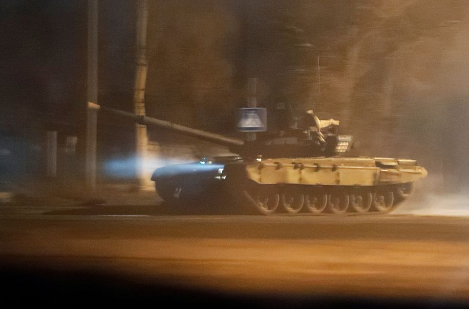 En bilde tatt gjennom litt tåke, eksos eller røyk viser en beltedrevet stridsvogn som kjører gjennom nattemørket.