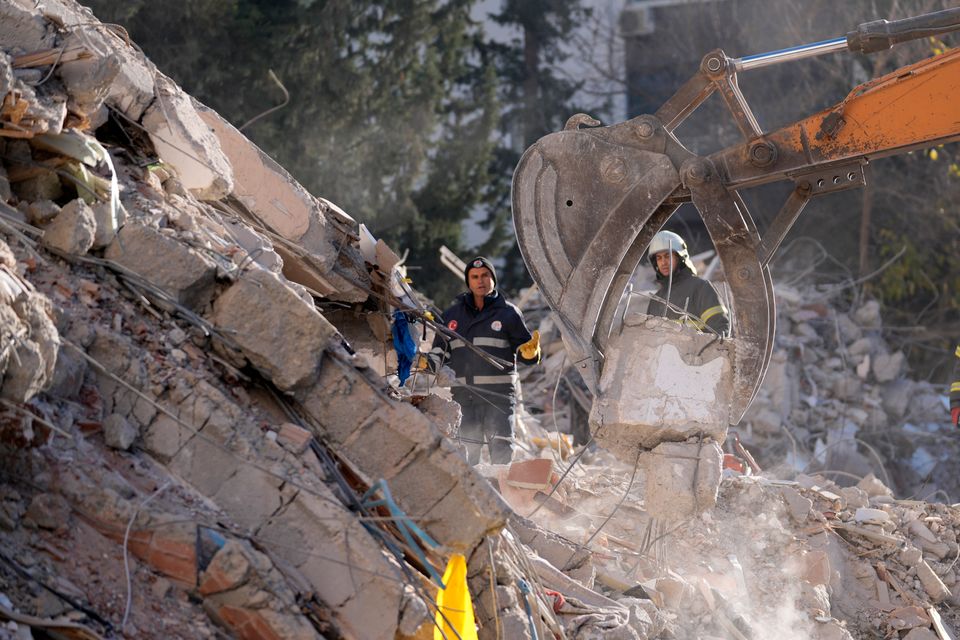 Flere mennesker leter mens en gravemaskin løfter noe et sted der en bygning har kollapset.