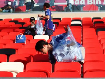 En mann med en stor plastsekk går rundt på en fotballstadion og plukker søppel.