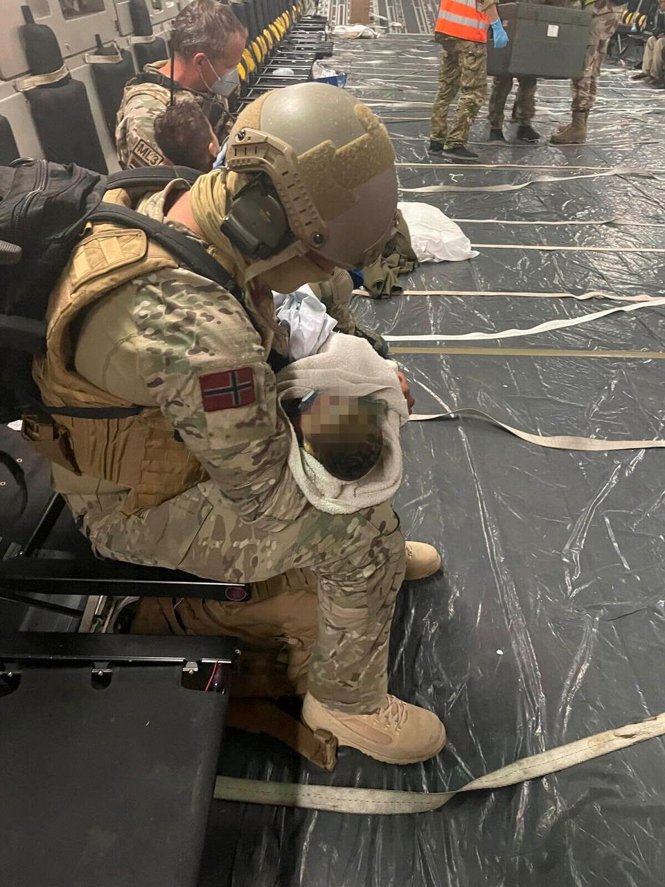 En soldat i uniform holder en baby i armene sine. 
