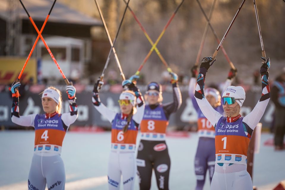 Mange kvinnelige skiløpere står i startområdet og holder stavene sine så de ser ut som et kors.