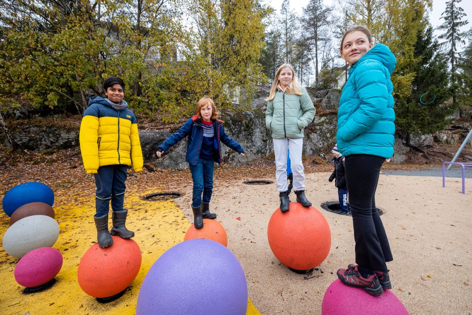 To gutter og to jenter balanserer oppå fargerike kuler i skolegården.
