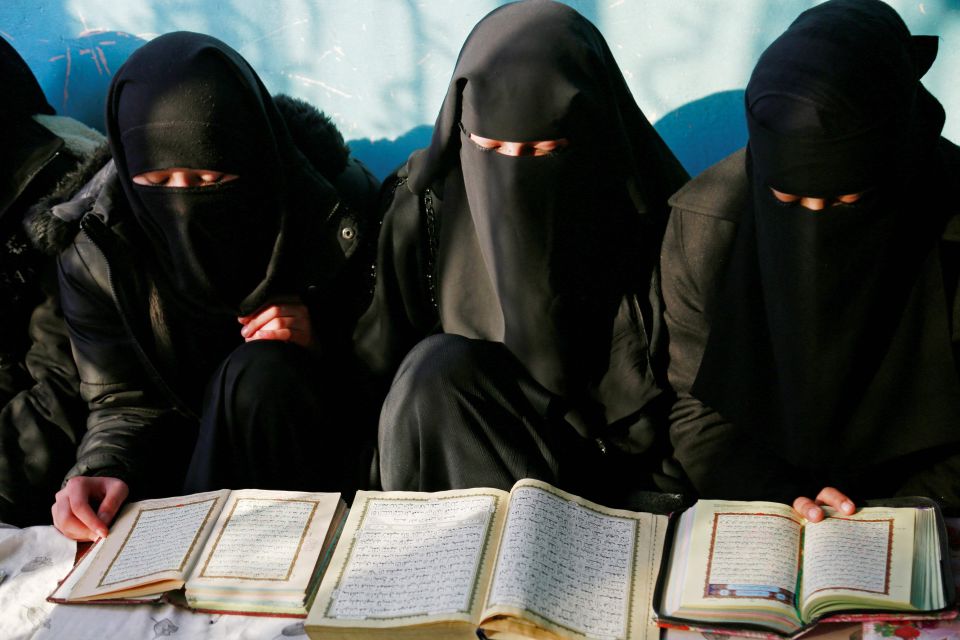 Tre kvinner med svarte klær som dekker dem helt sitter og leser i bøker.