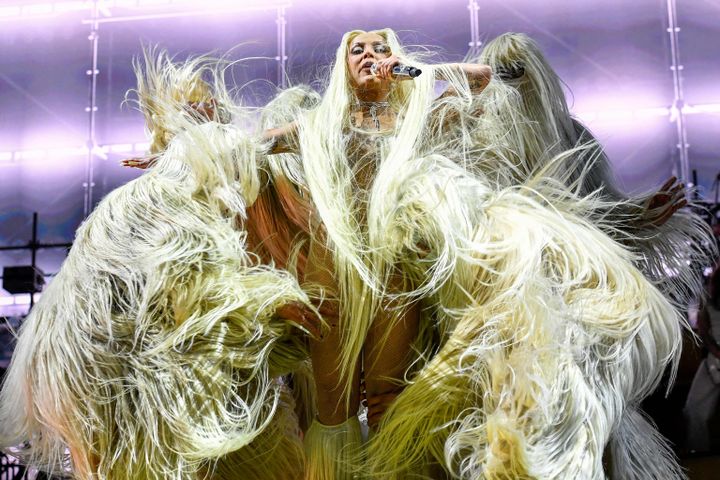 Dojo Cat, en rapper med langt, bleket hår og antrekk av parykker som ligner håret, danser mens hun holder en mikrofon, omgitt av dansere i drakter av lange, blonde parykker.