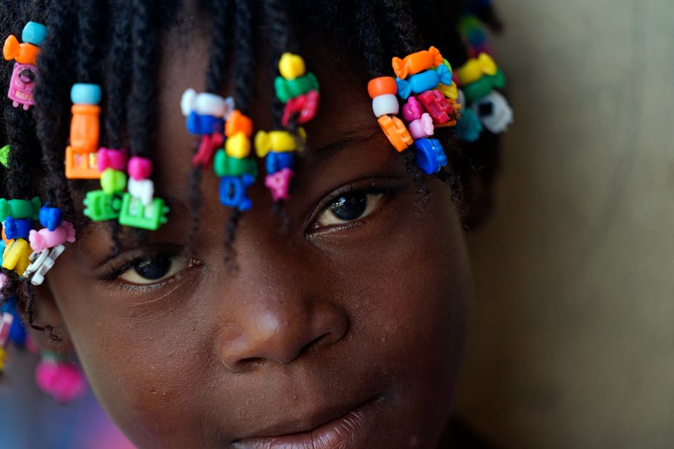En jente fra Haiti med perler i mange farger smiler til kamera. 