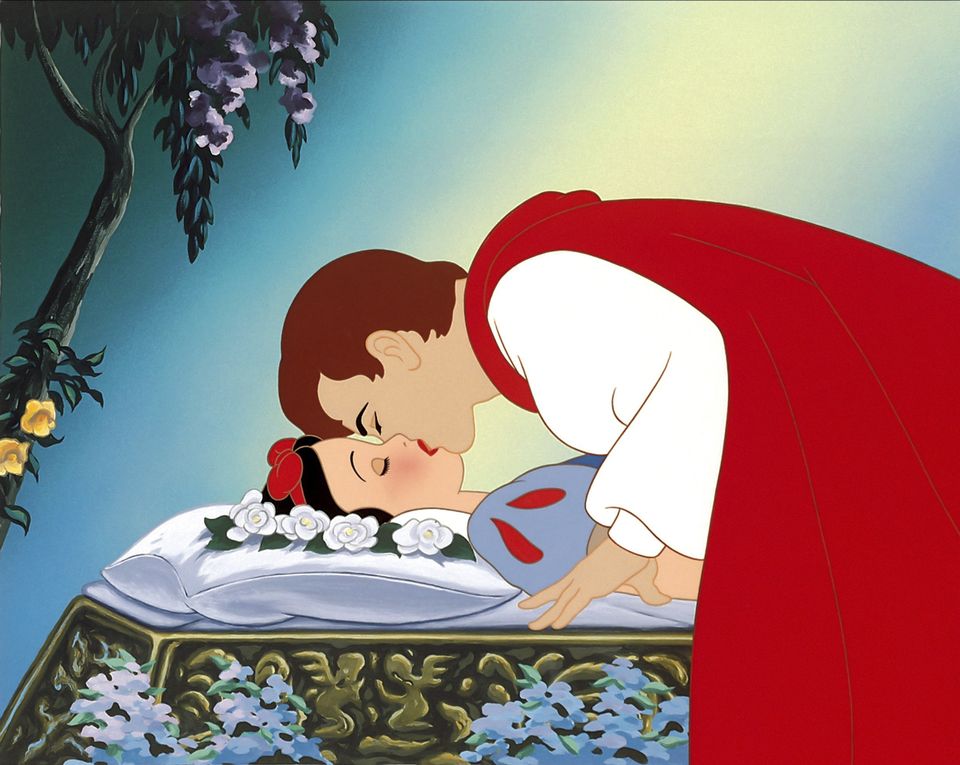 En scene fra filmen der Snehvit, en jente med svart hår og rød hårsløye, ligger oppå et podium mens prinsen, en mann med brunt hår, hvit skjorte og rød kappe kysser henne på munnen. 