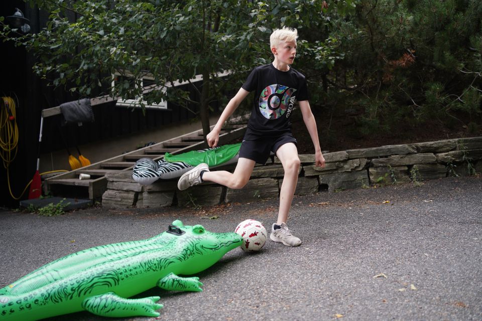 En grønn badeleke-krokodille er støtte til en fotball som en blond gutt er på vei til å skyte.