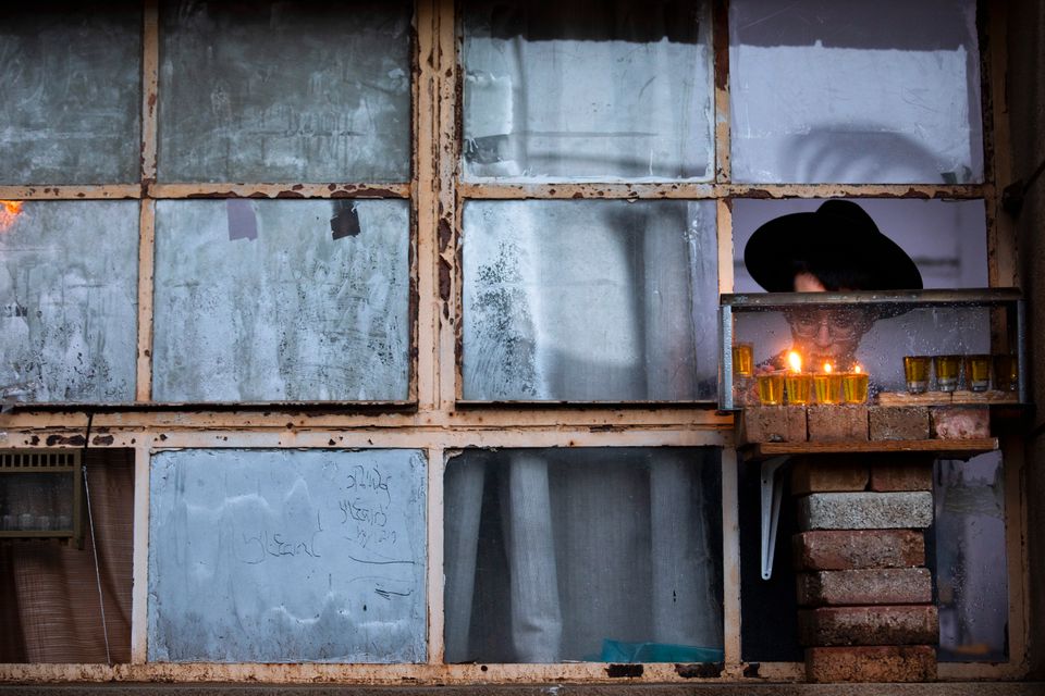 En gutt med svart hatt med brem, typisk for ultraortodokse jøder, tenner en rekke lyd i et vindu, mens det tilsynelatende mørkner utenfor. 