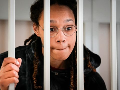 Kvinne med briller ser holder i og ser gjennom et fengselsgitter