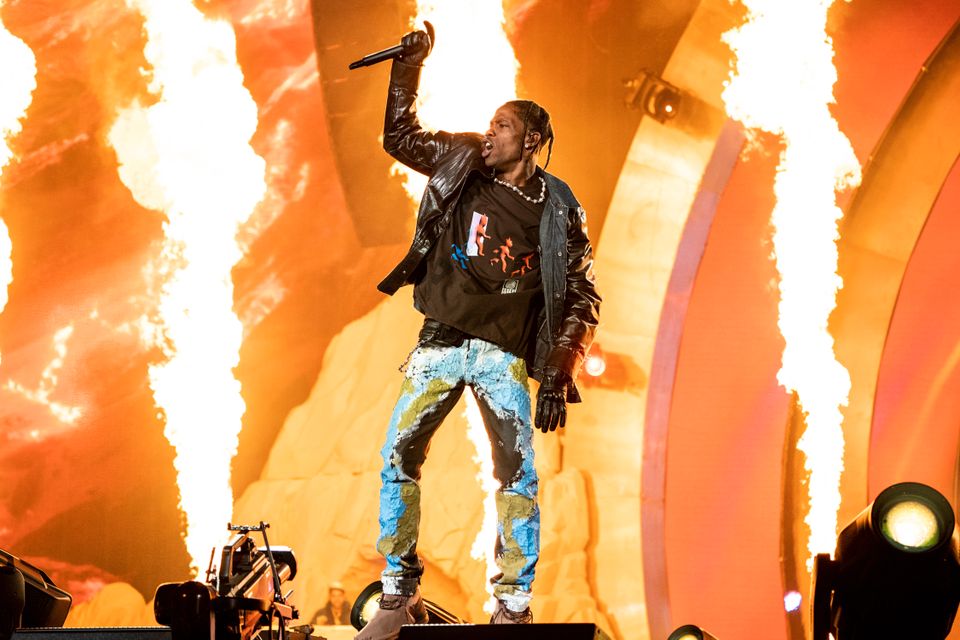 En artist med svart skinnjakke, hullete jeans, bokserfletter og mikrofonen løftet høyt i den høyre hånden står på en scene med pyroteknikk i bakgrunnen.