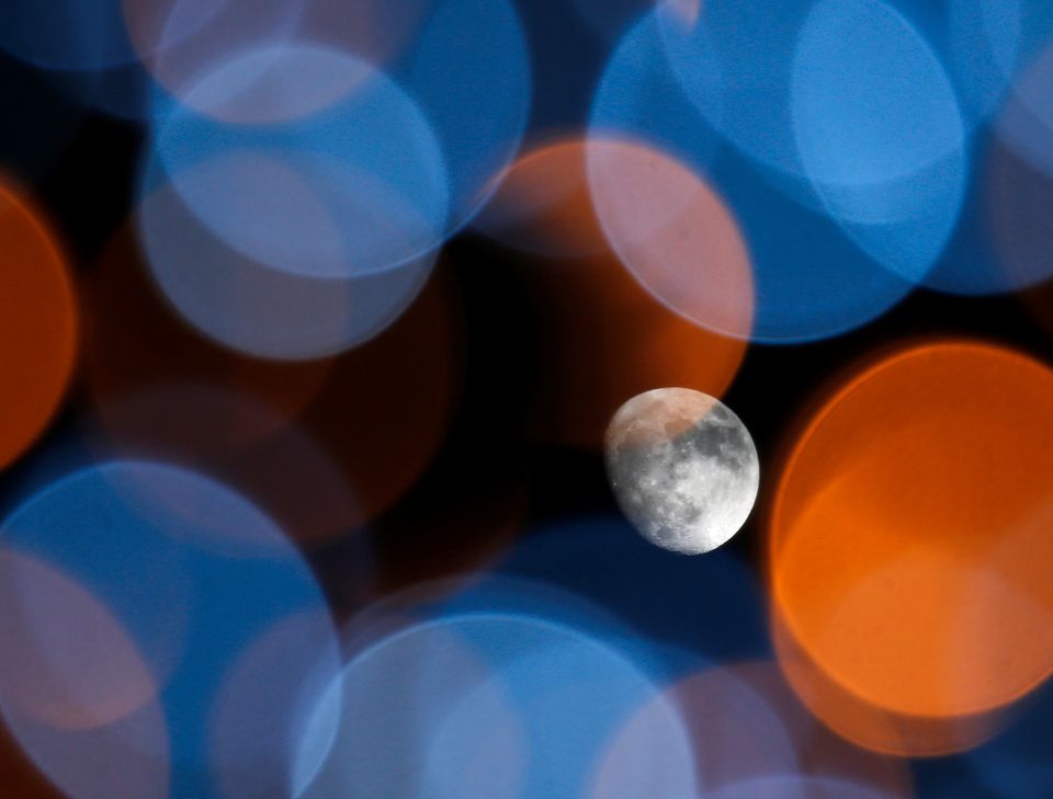 Bildet viser Månen mot en svart nattehimmel, sett gjennom uskarpe fargeflekker fra utendørs julelys.