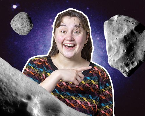 Tre grå og svarte asteroider er på hver sin side av en smilende jente med brunt hår og fargerik genser.