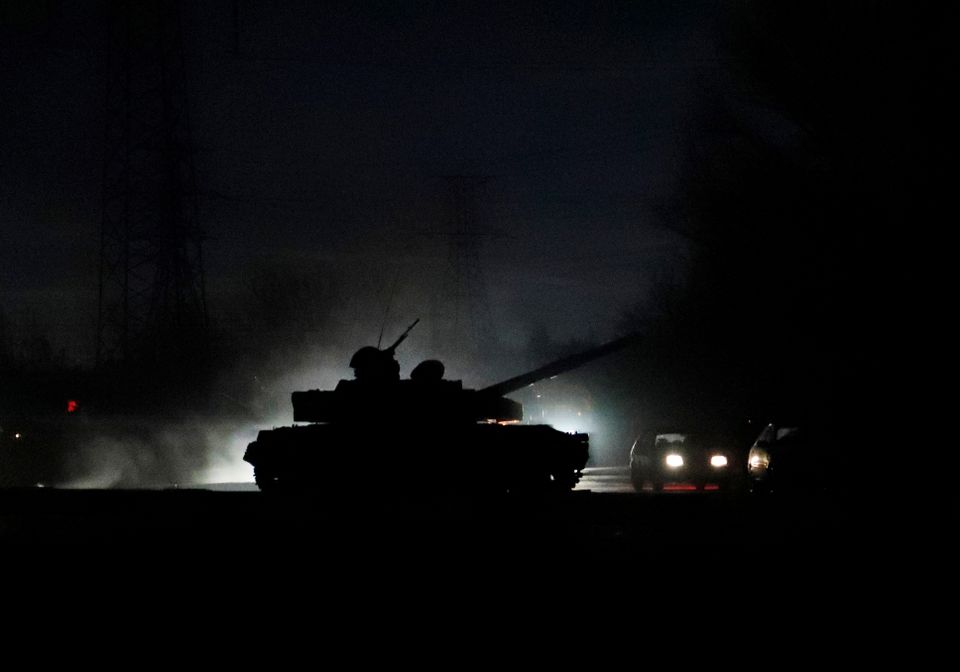 Et bilde tatt om natten viser silhuetten av en tanks som kjører med kanonen lett hevet. 