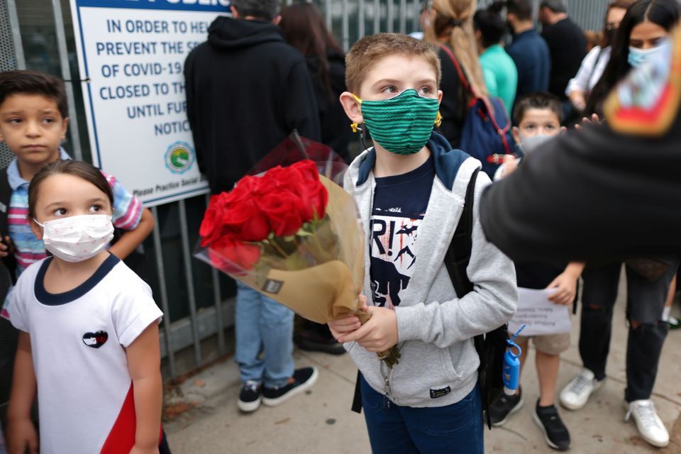 En skolegutt med grønt munnbind holder en bukett med røde roser. 