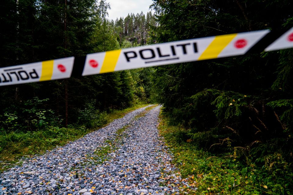 På en grusvei i en skog henger det et bånd som det står "Politi" på.