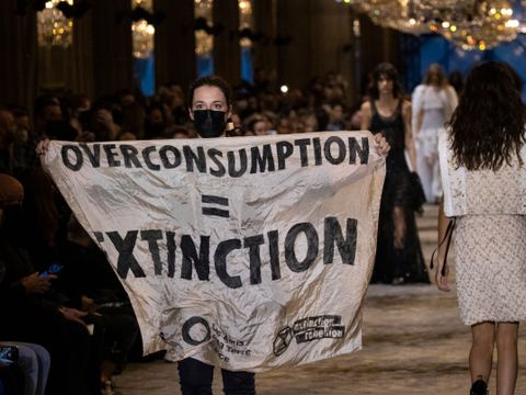 En aktivist med et banner i hendene går nedover en catwalk sammen med modeller.
